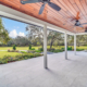 Covered patio with wood ceiling, ceiling fans, and stone tile flooring overlooking a landscaped lawn, garden beds, and mature trees in Orlando, Florida