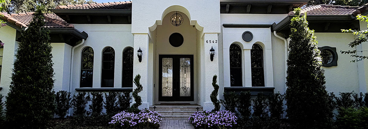 Mediterranean-style Orlando home with a landscaped front entrance, brick paver walkway, flowering garden beds, mature trees, and landscape lighting.