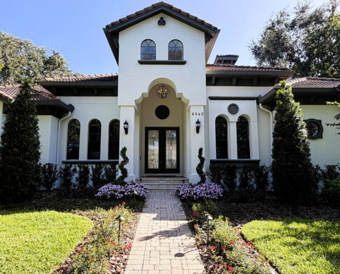 Mediterranean-style Orlando home with a landscaped front entrance, brick paver walkway, flowering garden beds, mature trees, and landscape lighting.
