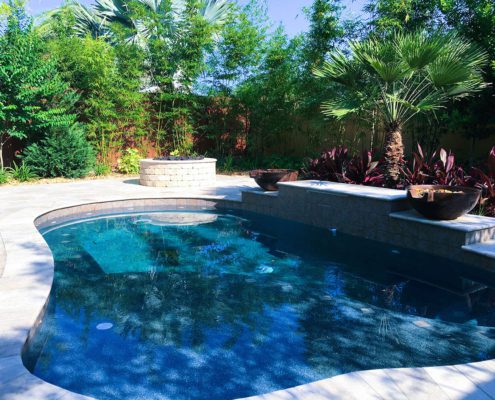 Orlando estate backyard pool with privacy landscaping, tropical palms, stone retaining wall, and integrated patio design