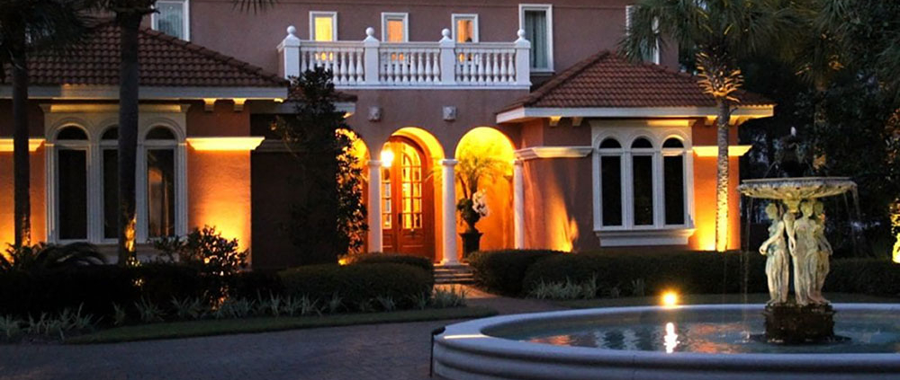Outdoor lighting illuminating a luxury home's entrance, palm trees, landscaping, and courtyard fountain. Orlando Landscape Design by BLG Environmental Services