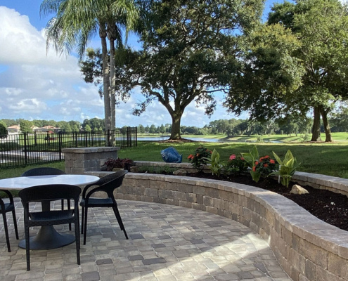Paver patio with outdoor dining furniture, curved stone planter walls, mature trees, and a lakefront view in the Orlando Florida area.