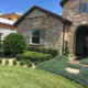 Front yard landscape design in Orlando, Florida featuring manicured hedges, ornamental trees, blue flowering groundcover, and a paver walkway leading to a stone-faced home.